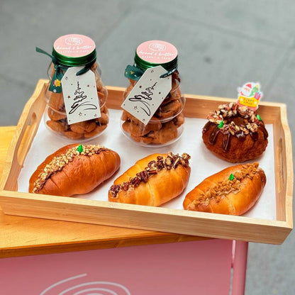 Wooden tray with pastries and jars labeled 'bread & butter' on a pink surface.